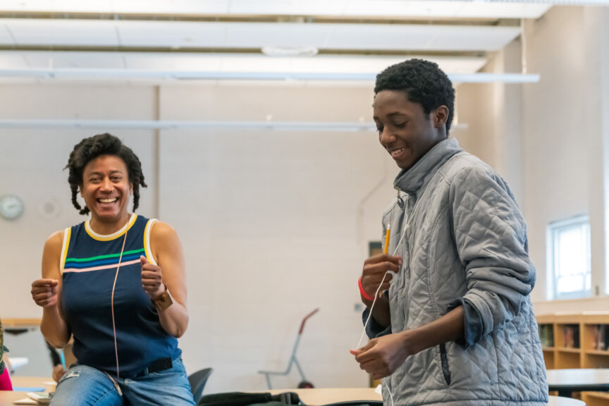 In classroom, Writer-in-Residence and student smile and laugh.