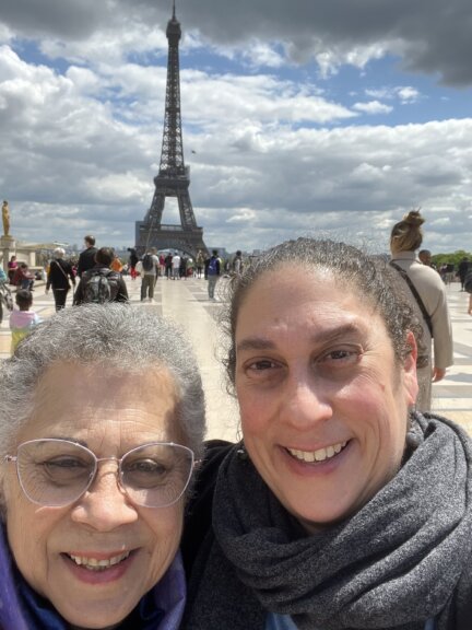 Suma and her mom pose in front of the Eiffel Tower. The sky is dappled with thick clouds.