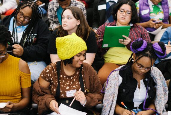 Group of teens sits in an auditorium talking and writing at the 2023 Detroit Youth Poetry Con