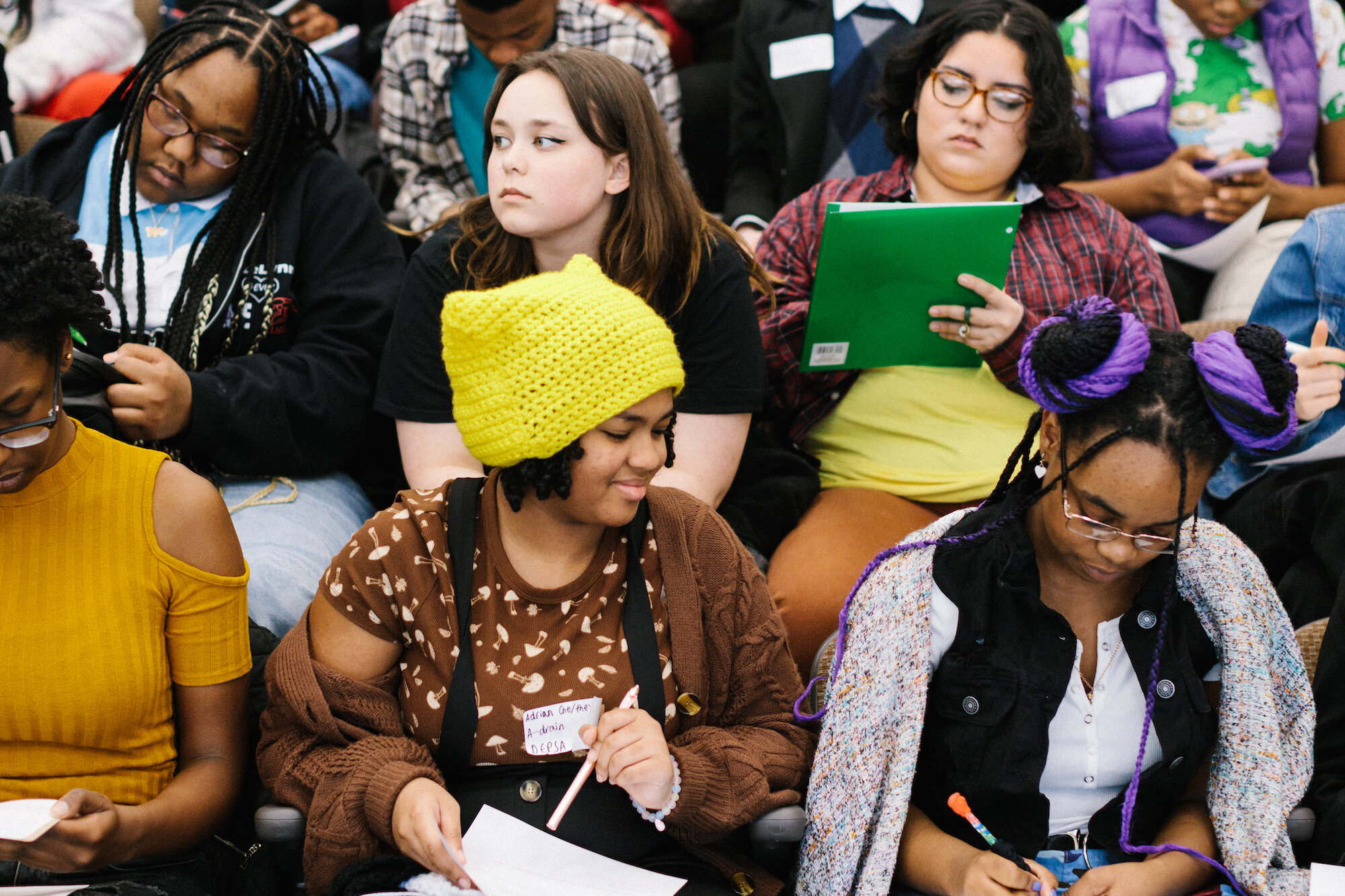 Group of teens sits in an auditorium talking and writing at the 2023 Detroit Youth Poetry Con
