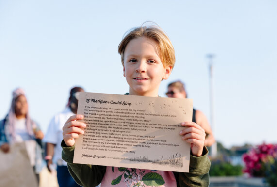 Youth poetry contest winner holds letterpressed poem outside at If the River Could Sing 2024.
