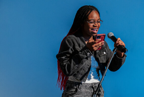 Student with long braids holds a microphone as she performs at a poetry slam.